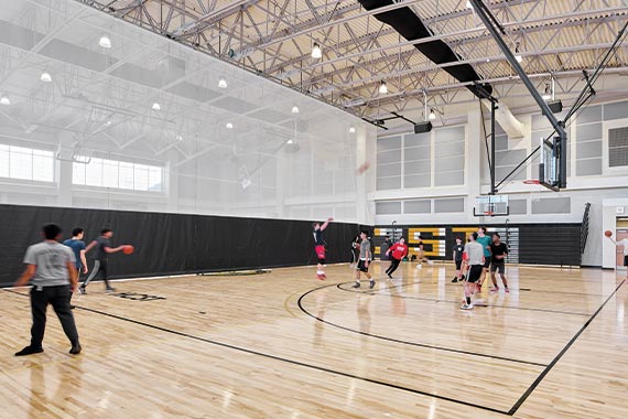 Students play a game of basketball at the Frank J. Gargiulo Campus. A fabric partition, separating the gymnasium into multiple courts, is down.